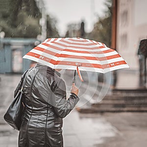 Rain. One elderly women under umbrella backs to us, lifestyle in city