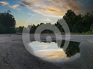 After rain puddle by the road with sky reflection on the surface