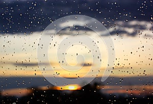 Rain at sunset. Wet window glass with raindrops against sun setting down. Autumn