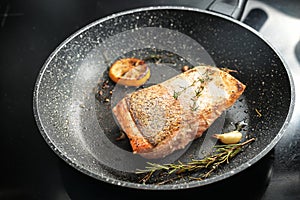 Rain trout fillet with a crispy fried skin, garlic, lemon and herbs in a frying pan, healthy cooking with fish, copy space,