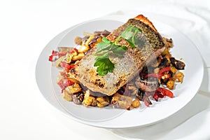 Rain trout fillet with a crispy fried skin on vegetables from the oven and parsley garnish served on a white plate, healthy fish