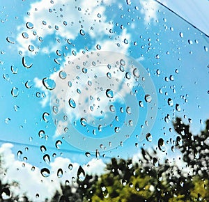 Rain water drops, blue sky, white clouds through window