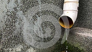 Rain water flows from a downpipe on the wall of a building close-up