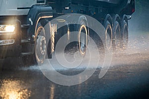 Rain water splash flow from wheels of heavy truck moving fast in daylight city with selective focus.