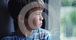 Rain, window and boy child thinking, sad and frustrated, depression and bored in his house. Mental health, winter