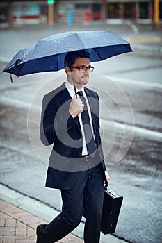 The rain wont hinder his focus on succeeding. Shot of a mature businessman holding an umbrella while out in the city.