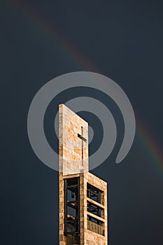 A rainbow above a modern church tower with christian cross, image with copy-space
