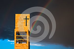 A rainbow above a modern church tower with christian cross, image with copy-space