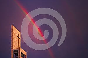 A rainbow above a modern church tower with christian cross, image with copy-space