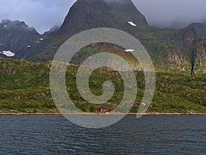 Rainbow above traditional wooden house with red facade on shore of Raftsundet strait on AustvÃ¥gÃ¸ya island, Lofoten, Norway.