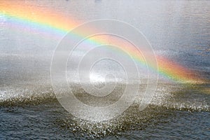 Rainbow above water surface. Rainbow from city fountain splash water drops