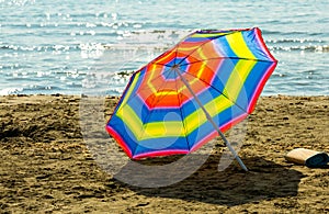 Rainbow beach umbrella on sand on the background of warm Mediterranean Sea in Cyprus Larnaca in summer