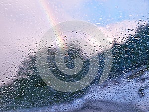 Rainbow behind car window glass with rain drops. After rain concept. Selective focus on window glass