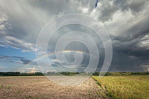 A rainbow in the cloudy sky over the rural fields