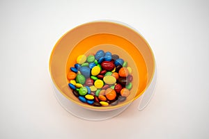 Rainbow Colored Candy Coated Chocolate Buttons in a orange bowl isolated on White