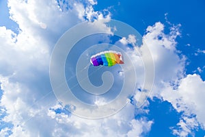 Rainbow colored child's kite on blue sky with clouds