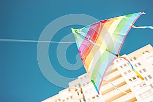 Rainbow colored kite flying in blue sky in city. Freedom and summer holiday concept