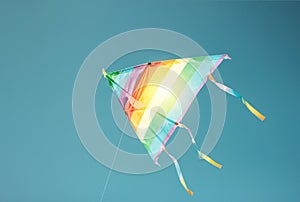 Rainbow colored kite flying in clean blue sky. Freedom and summer holiday