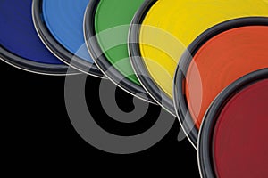 Rainbow colored paint can lids against black background