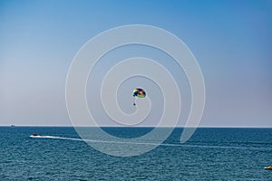 A rainbow-colored striped parachute with two passengers under it. People flying over the blue sea. Entertainment at the resort and