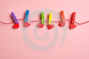 Rainbow colored wooden clothespins with clamped red hearts on pink background