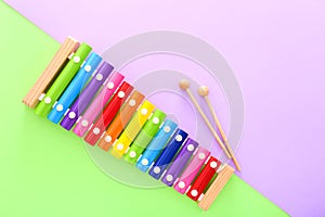 Rainbow colored wooden toy xylophone with two sticks on green and purple background. Top view