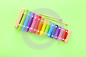 Rainbow colored wooden toy xylophone with two sticks on green background. Top view