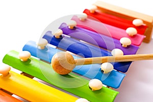 Rainbow colored wooden toy xylophone with two sticks on white background.