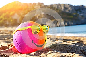 Rainbow colorful smiling beach ball dressed sunglasses on a sandy beach by tsea. Summer holidays concept