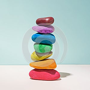 Rainbow colors natural stones piled on top of each other against blue sky and bright rose background. Minimal modern concept