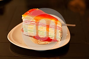 Rainbow crape cake on white plate on wood table.