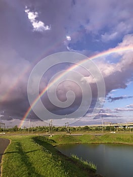 Rainbow double in the sky with clouds over the pond