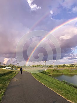 Rainbow double in the sky with clouds over the pond