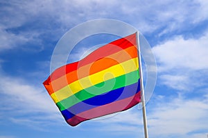 Rainbow flag of an LGBT organization waving against a blue sky. LGBT pride flags include lesbians, gays, bisexuals and