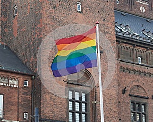 Rainbow Flag waving on metal flag pole in front of Copenhagen City Hall building, Denmark