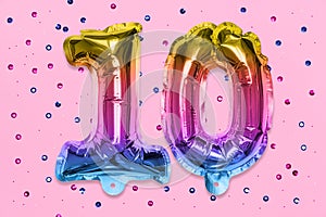 Rainbow foil balloon number, digit ten on a pink background with sequins. Birthday greeting card with inscription 10