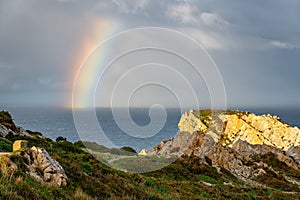 Rainbow formed by storms on the horizon of the sea seen from the cliffs of the shore, Asturias, Spain.