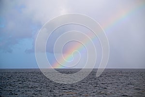 Rainbow in front of the sea with a blue cloudy sky in the background, perfect for wallpapers