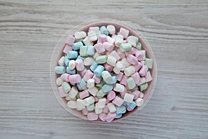 Rainbow Fruity Mini Marshmallows in a Pink Bowl on a white wooden background, top view. Flat lay, overhead, from above