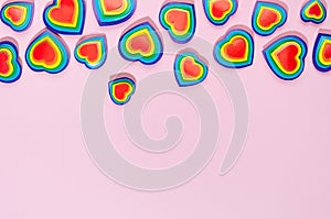 Rainbow hearts on pastel pink background, decorative border, copy space, top view.