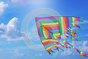 Rainbow kite flying in blue sky with clouds. Freedom and summer holiday