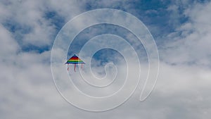 Rainbow kite hovers in the blue sky with white clouds.