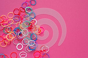 Rainbow loom bands bracelets on pink background. Colorful ties for waving hair. Children hobby - handmade bracelets