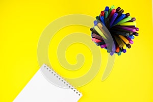 Rainbow markers with Notepad isolated on a yellow background top view