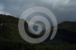 Rainbow between Monserrate and Guadalupe hills in colombian capital Bogota with cloud forest mountains trees