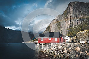 Rainbow ofer red houses rorbuer of Reine in Lofoten, Norway with red rorbu houses, clouds, rainy blue sky and sunny