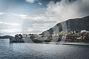 Rainbow ofer red houses rorbuer of Reine in Lofoten, Norway with red rorbu houses, clouds, rainy blue sky and sunny