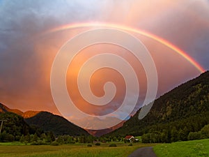 Rainbow by orange clouded sky in alpine landscape