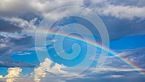 Rainbow over blue sky with clouds.