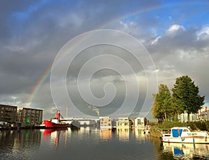 Rainbow over cloudy sky above harbour with light house boat